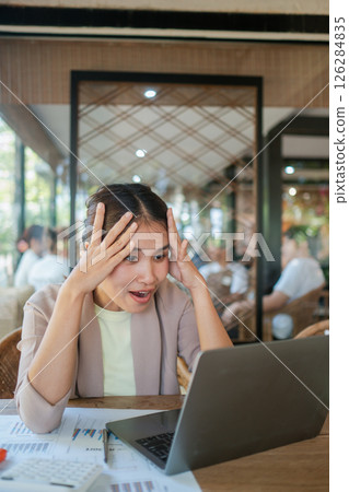 A businesswoman reacts with surprise while viewing positive results on her laptop in a modern cafe environment. A businesswoman reacts with surprise while viewing positive results on her laptop in a modern cafe environment. 126284835