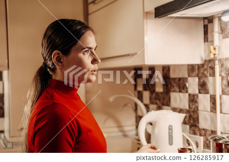 Woman Kitchen Night Kettle: Concerned woman holds electric kettle in dimly lit kitchen at night. 126285917