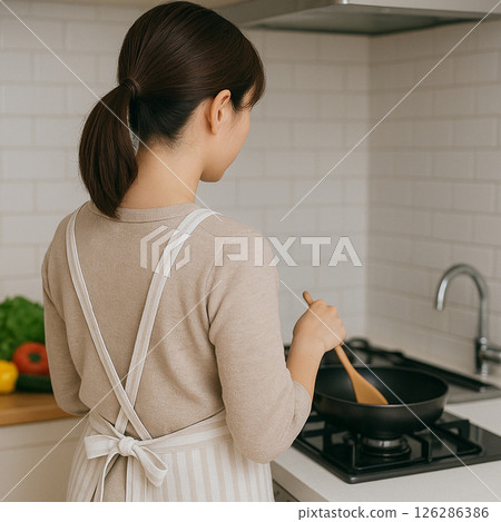 一位繫著圍裙的女子在廚房做飯 126286386