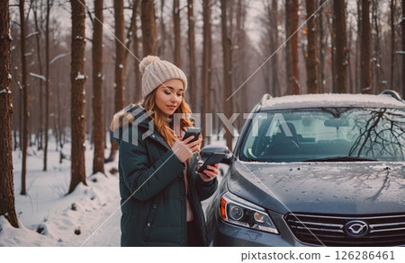 Woman is standing in the snow, looking at her phone. She is wearing a hat and a green jacket Woman is standing in the snow, looking at her phone. She is wearing a hat and a green jacket 126286461