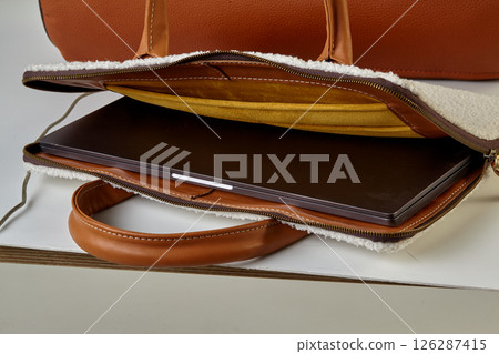 Stylish leather laptop sleeve protecting modern ultrabook on white table Stylish leather laptop sleeve protecting modern ultrabook on white table 126287415