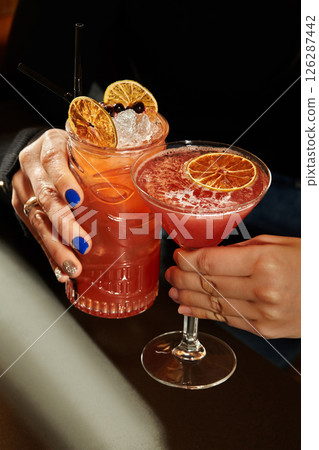Women holding tropical tiki cocktails with dehydrated orange slices and ice cubes Women holding tropical tiki cocktails with dehydrated orange slices and ice cubes 126287442