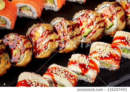 Tempura and eel sushi rolls with salmon and avocado filling resting on a black stone plate 126287493