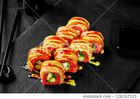 Sushi rolls covered with salmon and sauce lying on black stone plate 126287523