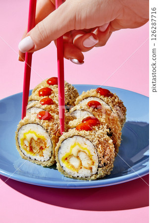 Woman picking breaded sushi roll with pink chopsticks on blue plate Woman picking breaded sushi roll with pink chopsticks on blue plate 126287716