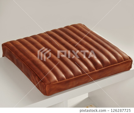 Comfortable brown leather seat cushion resting on white bench 126287725