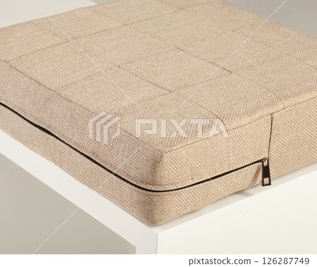 Beige fabric cushion resting on white surface with zipper detail Beige fabric cushion resting on white surface with zipper detail 126287749