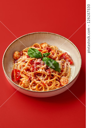 Delicious italian spaghetti with tomato sauce, basil, and cheese on red background Delicious italian spaghetti with tomato sauce, basil, and cheese on red background 126287830
