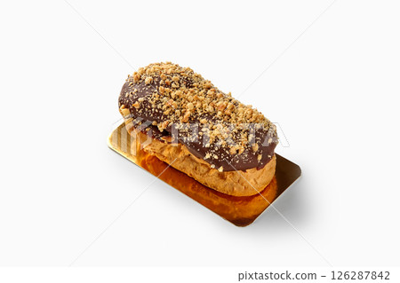 Delicious eclair covered with chocolate and peanuts resting on golden tray 126287842