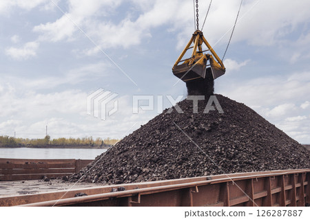 Loading coal using a floating crane onto a barge. Coal is poured from a bucket onto a barge, the Yenisei River. Loading coal using a floating crane onto a barge. Coal is poured from a bucket onto a barge, the Yenisei River. 126287887