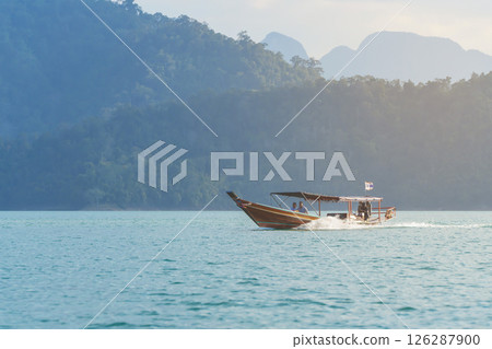 Boating and water tourism in Thailand - A longtail with tourists sailing on Cheo Lan Lake against the backdrop of high mountains 126287900