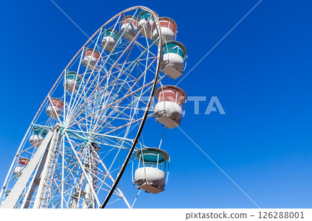 Colorful ferris wheel cabins captured under a vibrant blue sky 126288001