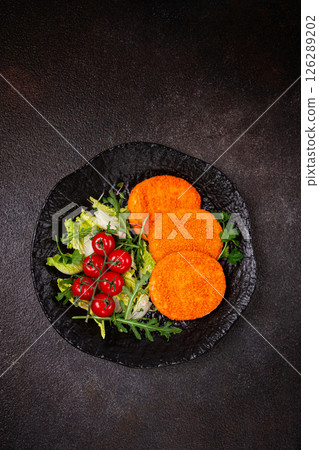 crispy fried fish cutlets, fish burgers, on a black plate, with fresh lettuce leaves, arugula and cherry tomatoes, homemade, no people, 126289202