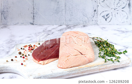 Fresh raw duck breasts, spread on a wooden cutting board, with herbs and spices, on a white marble surface Fresh raw duck breasts, spread on a wooden cutting board, with herbs and spices, on a white marble surface 126289208