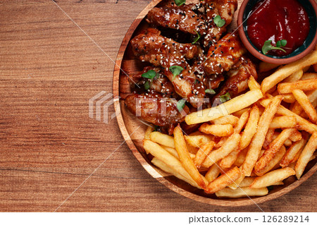 barbecue chicken wings, sprinkled with sesame seeds, with French fries, and sauce, on a wooden plate, rustic style, 126289214