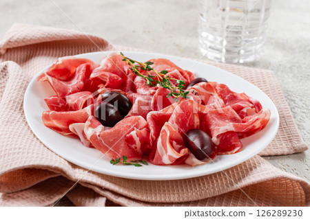 Freshly cut dried meat, served with olives and herbs, on a white plate, light background, no people, Freshly cut dried meat, served with olives and herbs, on a white plate, light background, no people, 126289230