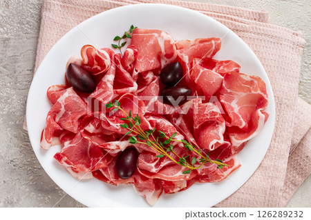 Freshly cut dried meat, served with olives and herbs, on a white plate, light background, no people, 126289232