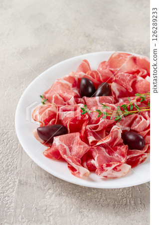 Freshly cut dried meat, served with olives and herbs, on a white plate, light background, no people, 126289233