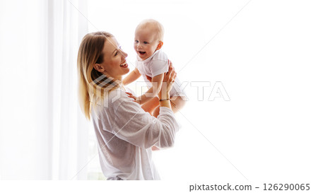 Joyful young mother and baby dressed in white laughing and playing together, tickling and bonding on white background. Beautiful mom and small child in arms Joyful young mother and baby dressed in white laughing and playing together, tickling and bonding on white background. Beautiful mom and small child in arms 126290065