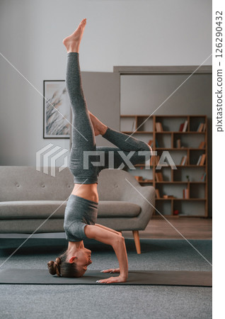 Making headstand. Young woman in yoga clothes doing fitness indoors Making headstand. Young woman in yoga clothes doing fitness indoors 126290432