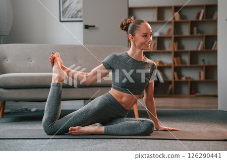 Stretching the legs. Young woman in yoga clothes doing fitness indoors Stretching the legs. Young woman in yoga clothes doing fitness indoors 126290441