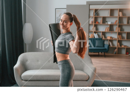 Posing, holding mat. Young woman in yoga clothes doing fitness indoors Posing, holding mat. Young woman in yoga clothes doing fitness indoors 126290467