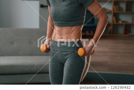 Holding dumbbells. Young woman in yoga clothes doing fitness indoors 126290482