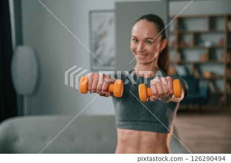 Positive young woman in yoga clothes is smiling and holding dumbbells 126290494