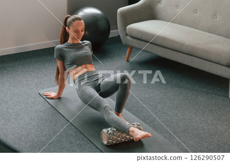 Leg are on the foam roller. Young woman in yoga clothes doing fitness indoors 126290507