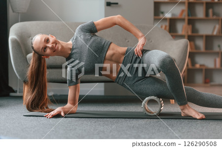 Leg are on the foam roller. Young woman in yoga clothes doing fitness indoors 126290508