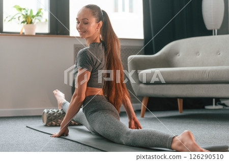 Big stretch for legs. Young woman in yoga clothes doing fitness indoors 126290510