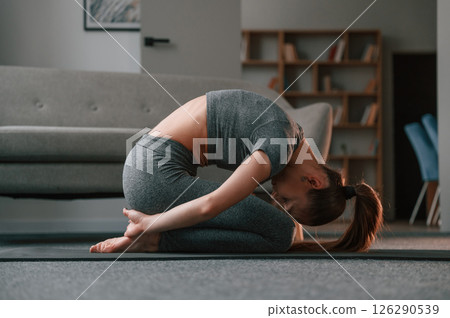 Focused on stretching exercise. Young woman in yoga clothes doing fitness indoors 126290539