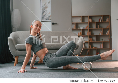 Legs exercises by using foam roller. Young woman in yoga clothes doing fitness indoors 126290556
