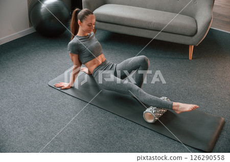 Legs exercises by using foam roller. Young woman in yoga clothes doing fitness indoors 126290558