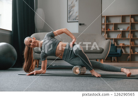 On the right hand and leg on the foam roller. Young woman in yoga clothes doing fitness indoors On the right hand and leg on the foam roller. Young woman in yoga clothes doing fitness indoors 126290565