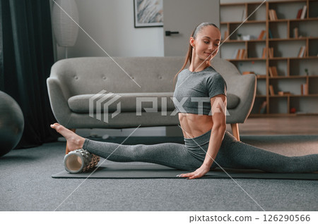 On the mat with foam roller. Young woman in yoga clothes doing fitness indoors 126290566