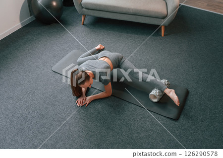On the mat with foam roller. Young woman in yoga clothes doing fitness indoors 126290578