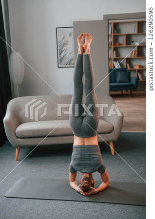 Standing upside down. Young woman in yoga clothes doing fitness indoors Standing upside down. Young woman in yoga clothes doing fitness indoors 126290596