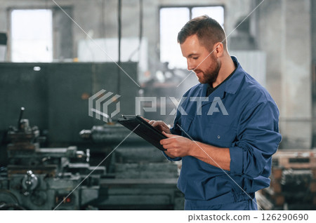 Front view. Factory worker in blue uniform is indoors 126290690