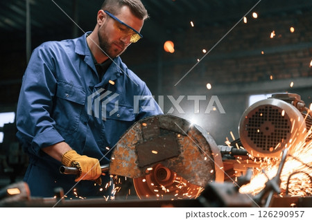 Many of the sparks. Welding the metal. Factory worker in blue uniform is indoors 126290957