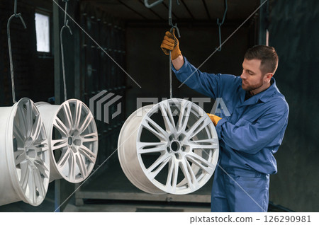 Disk of wheels are hanging. Car service station worker is indoors 126290981