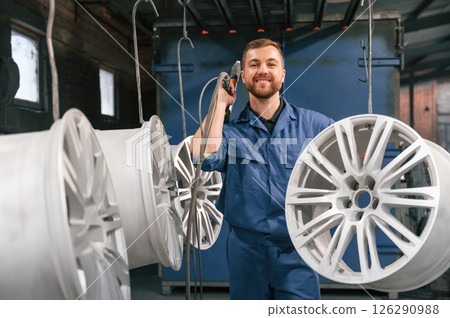 Holding paint spray gun. Car service station worker is taking care about disks of tires Holding paint spray gun. Car service station worker is taking care about disks of tires 126290988
