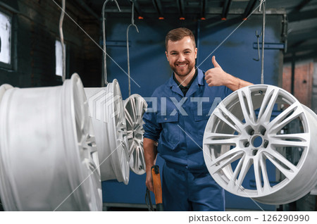 Showing thumb up. Car service station worker is taking care about disks of tires 126290990