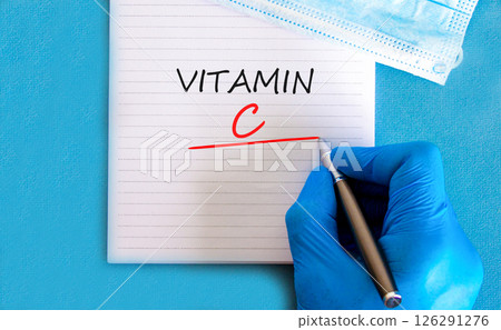 Vitamin C symbol. Concept words Vitamin C on beautiful white note. Doctor's hand in blue medical glove. Medical mask. Beautiful blue background. Medical healthy lifestyle Vitamin C concept. Vitamin C symbol. Concept words Vitamin C on beautiful white note. Doctor's hand in blue medical glove. Medical mask. Beautiful blue background. Medical healthy lifestyle Vitamin C concept. 126291276
