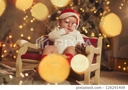 Sitting on the little sofa. Cute baby is at home. New year decorations. Conception of holidays Sitting on the little sofa. Cute baby is at home. New year decorations. Conception of holidays 126291409
