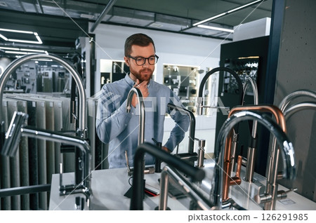 A large selection of water faucets. Man chooses a products in a sanitary ware store A large selection of water faucets. Man chooses a products in a sanitary ware store 126291985