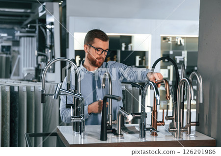 A large selection of water faucets. Man chooses a products in a sanitary ware store A large selection of water faucets. Man chooses a products in a sanitary ware store 126291986