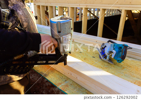Contractor worker applies nail gun to wooden beams while working on construction project 126292002