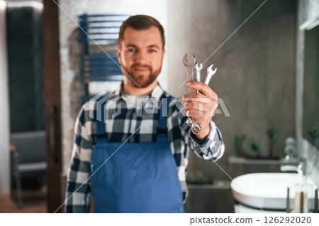 Holding wrenches. Plumber in blue uniform is at work in the bathroom Holding wrenches. Plumber in blue uniform is at work in the bathroom 126292020