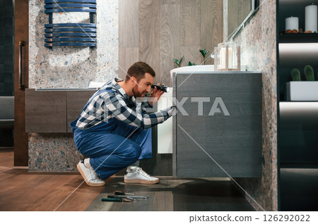 Plumber in blue uniform is at work in the bathroom 126292022